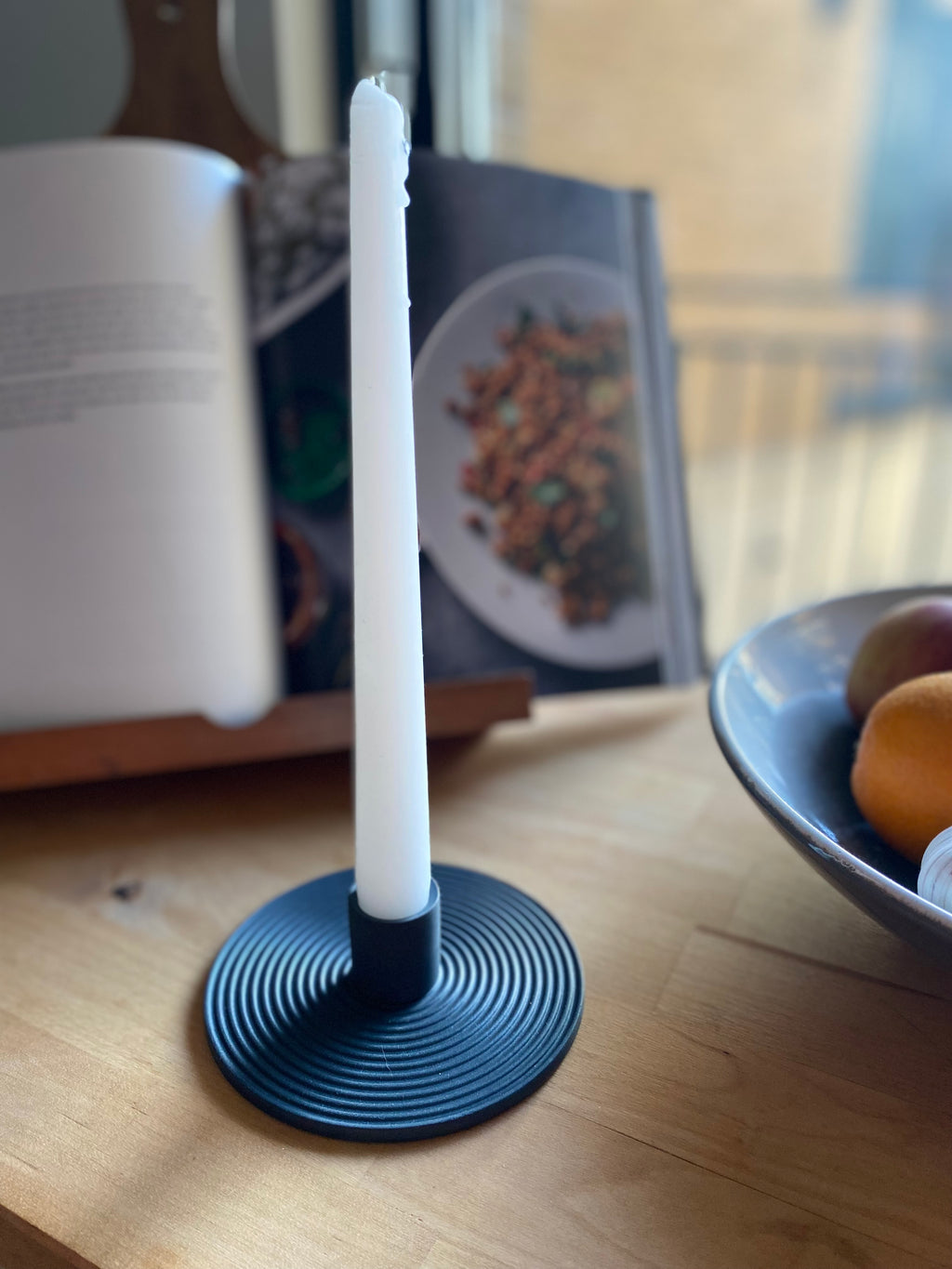 White candle in a black holder on a wooden surface with a blurred background