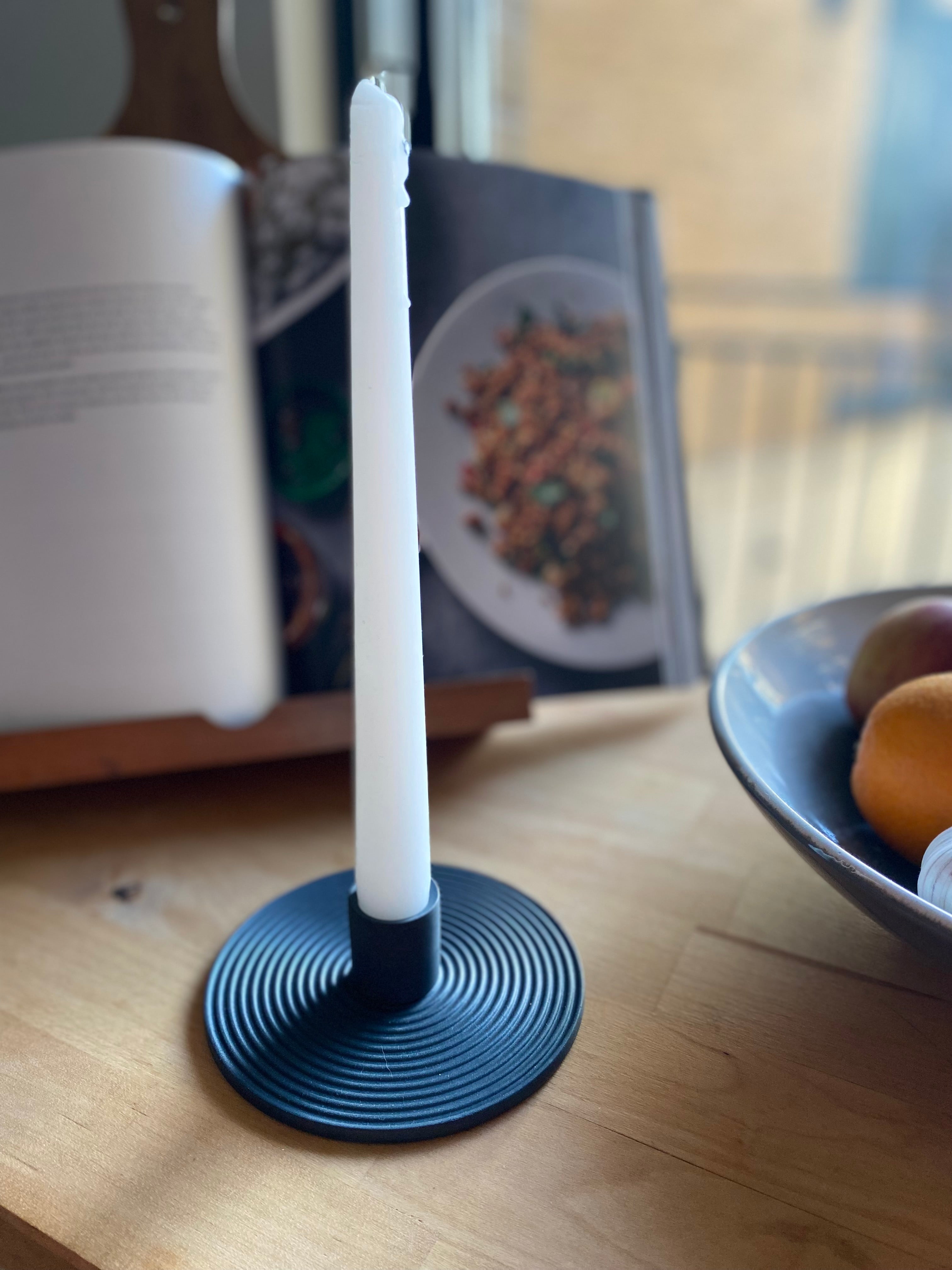 White candle in a black holder on a wooden surface with a blurred background