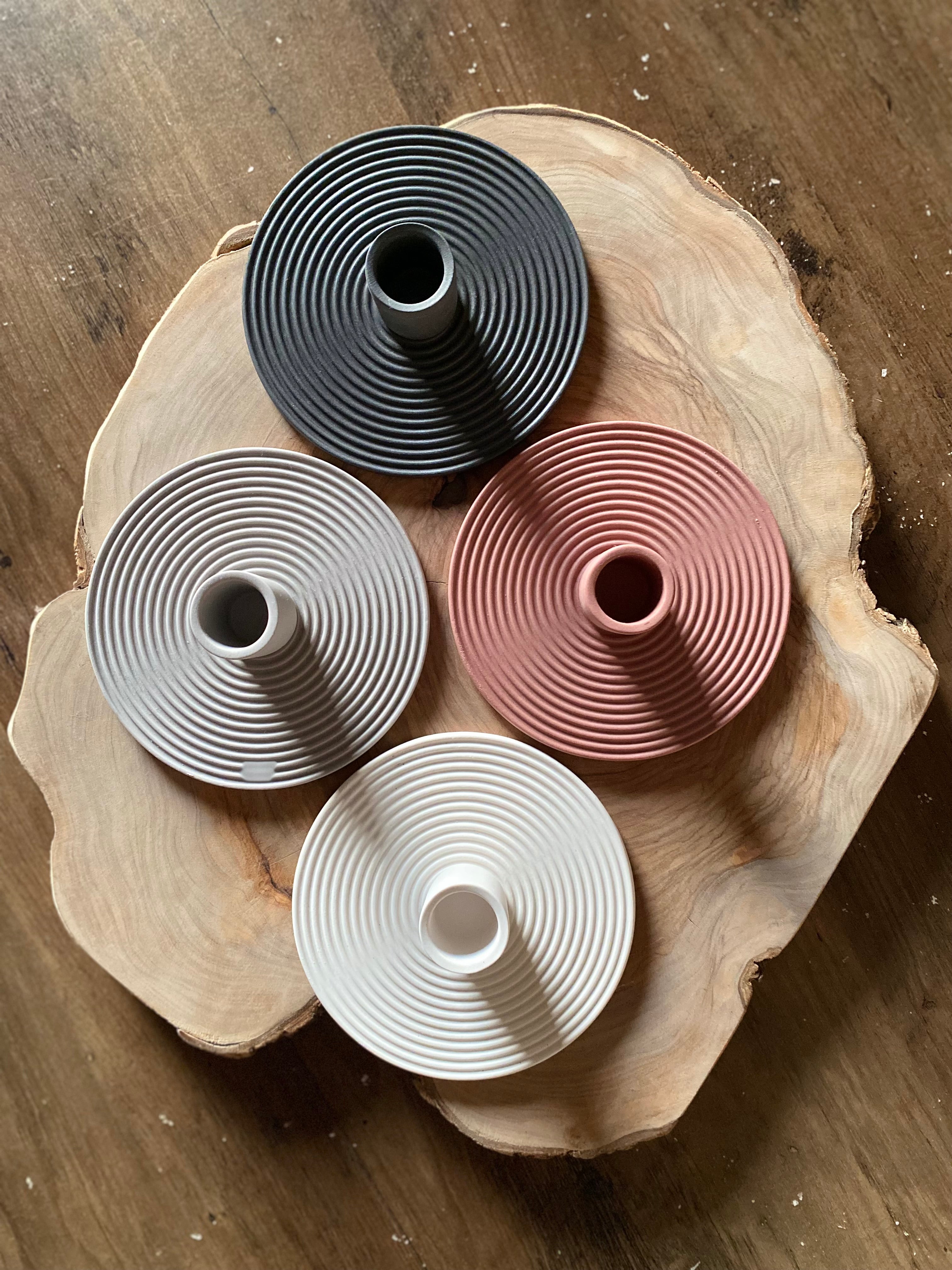 Four ceramic candle holders in black, grey, pink, and white on a wooden surface.